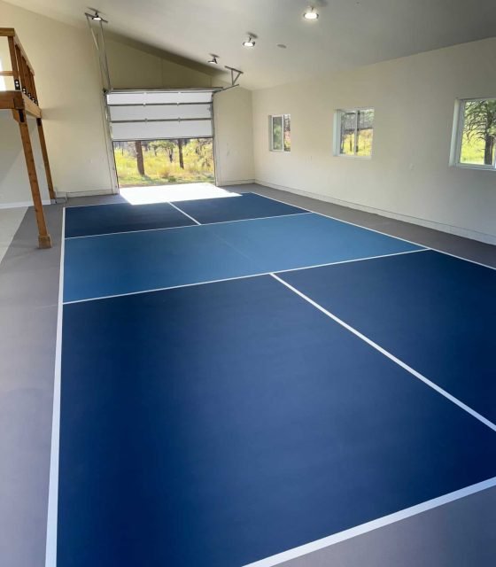 Bright blue tennis court surface with crisp white lines in a spacious indoor facility.